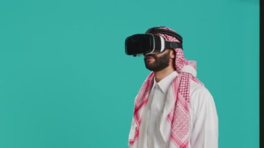 Stüdyoda VR kulaklık kullanan Ortadoğulu bir adam interaktif gözlüklü sanal gerçeklik teknolojisiyle çekimlerin tadını çıkarıyor. 3 boyutlu simülasyon, modern hobi ve aletlerle eğlenen genç insan.