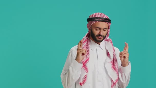 穆斯林男子双手交叉双手 在蓝色的背景下为真主祈祷 展示宗教和精神信仰 穿着伊斯兰服装的年轻人信奉宗教 虔诚地崇拜上帝 — 图库视频影像