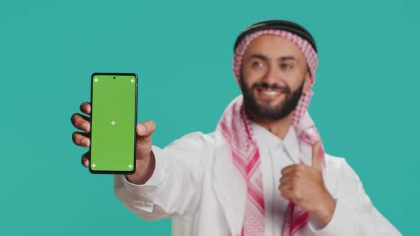 モバイルデバイス上のムスリム男性 緑色のテーマ スマートフォンディスプレイに隔離されたモックアップ染色を先に置く 若いアラビア人が空白のコピースペーステンプレートデザインを展示 — ストック動画