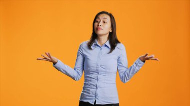 Kameranın karşısında omuzlarını kaldıran cahil bir insan şüpheyi dile getiriyor ve cevaptan emin olamıyor. Genç Asyalı kadın turuncu arka plana karşı durarak kendinden emin ve şaşkın davranıyor..