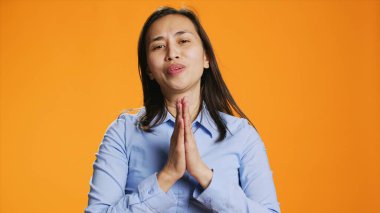 Filipinli model affedilmek ve kamerada minnettarlık göstermek için dua ediyor, maneviyata inanan umut dolu bir kadın. Dua eden Asyalı birinin Tanrı 'ya inancı var, turuncu arka plan..