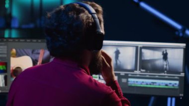 Yaratıcı ofiste renk dengesi ve ışıklandırma düzenlemeden önce film montajını analiz eden video editörü. Yapım stüdyosu çalışanı kulaklıkla müzik dinlerken ham görüntülerle çalışıyor.