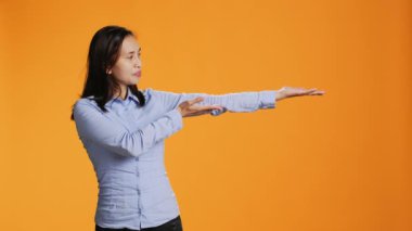 Filipinli kadın stüdyonun her iki tarafına da bir şey gösteriyor, turuncu arka planda pazarlama reklamı sunuyor. Genç yetişkin yeni reklam reklamı için sağı solu işaret ediyor.