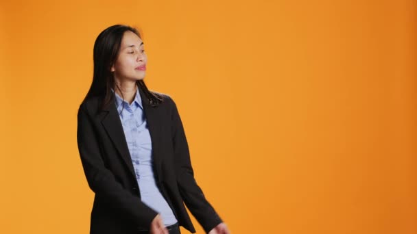 アジアの従業員は スタジオの左側または右側を指し オレンジ色の背景に新しいWebコマーシャルを作成します 撮影中にマーケティング広告に取り組む若手ビジネスマネージャー — ストック動画