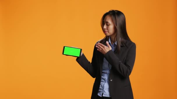 女商人手持带有绿屏模板的手机 在橙色背景下摆出姿势 并在工作室中显示空白的复制空间 智能手机应用上有铬色屏幕的亚洲成年人 — 图库视频影像