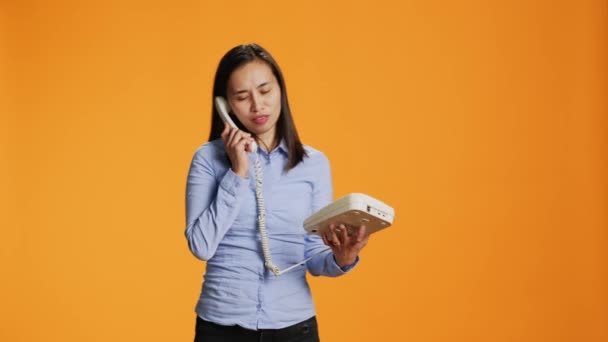 アジアの人は 彼女が古いファッションライン上の誰かに話すように 地上電話で遠隔電話をしている ケーブルでオフィスの電話を扱う自信のある女性 リモートでスタジオで対話 — ストック動画