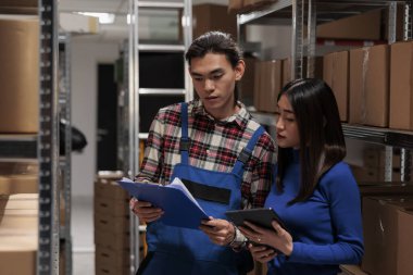 Posta deposunda hisse senedi kontrolü yapan Asyalı nakliye müdürleri. Depo çalışanları ve kadın işçiler ürün listesini panodan kontrol ediyor ve dijital tablette lojistik analizi yapıyorlar.