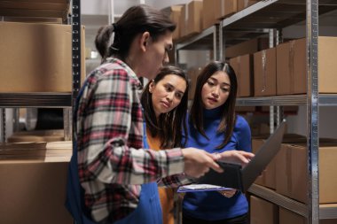 Depo personeli depoda lojistik ve dağıtım işlerini yürütüyor. Depoda çalışan Asyalı erkek ve kadın işçiler dizüstü bilgisayardan ürün kalite kontrol raporlarını birlikte kontrol ediyorlar.