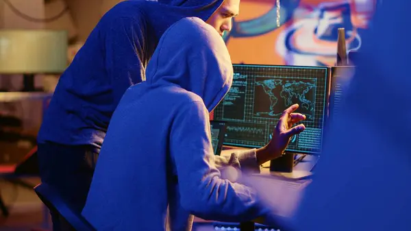 stock image Hacking group founder initiating new member, showing him how to destroy firewalls and infect victim computer in hideout. Evil cybersecurity guru teaches script kiddie how to write malware code