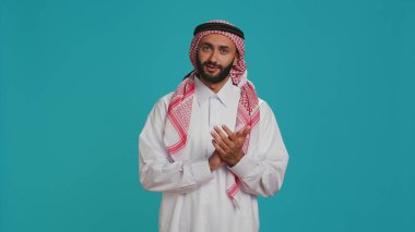 Geleneksel cüppeli Müslüman yetişkinler stüdyoda alkışlarken destek veriyorlar. Orta Doğulu adam beyaz tobe ve başörtüsü takıyor, alkışlıyor ve tezahürat yapıyor..