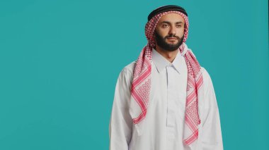 Geleneksel giyinmiş, gülümseyen ve kendine güvenen orta doğulu bir adam, damalı baskılı başörtüsü ve beyaz bornozla Arap kültürel kimliğini temsil ediyor. Genç, neşeli Arap..