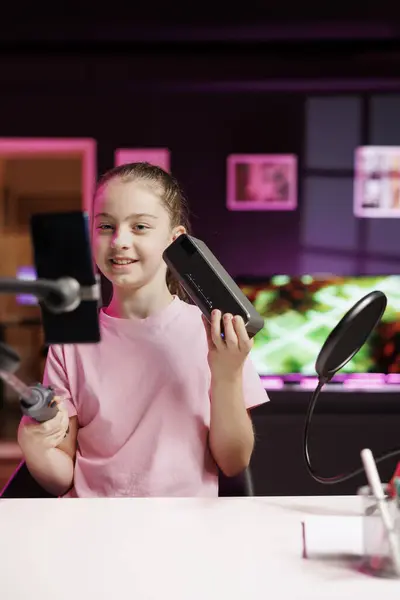 Gen Z media star filming video about best portable speaker launched this year with phone on selfie stick. Kid tech content creator recording music playing device review using smartphone camera