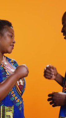 Dikey Video Genç Afrikalı Amerikalılar kameraya yumruk tokuşturarak birbirlerini modern jestlerle selamlıyorlar. Geleneksel kıyafetlerle gülümseyen karı koca stüdyoda poz veriyor.