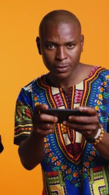 Dikey Video Etnik çifti telefondaki mobil video oyunlarıyla eğleniyor, kameradaki online oyun turnuvasına katılıyorlar. Afrika kökenli Amerikalı erkek ve kadın akıllı telefondan oyun yarışmasında oynuyorlar..