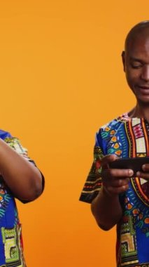 Dikey Video Afrikalı Amerikalılar mobil cihazda video oyunu oynuyorlar, stüdyoda online oyun yarışmalarıyla eğleniyorlar. Evli erkek ve kadın akıllı telefon uygulamasında oyun turnuvasının tadını çıkarıyorlar..