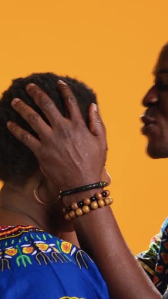 垂直ビデオ アフリカ系アメリカ人男性 カメラに妻の額にキスし 彼女の甘い愛情のために誠実な気持ちを表現します 夫はスタジオでロマンチックなジェスチャーをして 彼のことを気にかけます — ストック動画