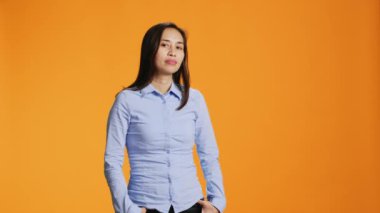 Turuncu arka planda duran gülümseyen genç bir kadın. Stüdyoda özgüvenli ve tasasız hissediyor. Filipinli biri kamerada şık kıyafetler ile poz veriyor, güzel bir kadın model..