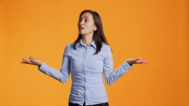 Kameranın karşısında omuzlarını kaldıran cahil bir insan şüpheyi dile getiriyor ve cevaptan emin olamıyor. Genç Asyalı kadın turuncu arka plana karşı durarak kendinden emin ve şaşkın davranıyor..