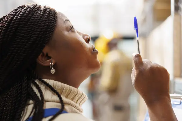 Afrykański Amerykański Kierownik Magazynu Patrząc Górę Wskazując Długopisem Kierowniczka Magazynu — Zdjęcie stockowe