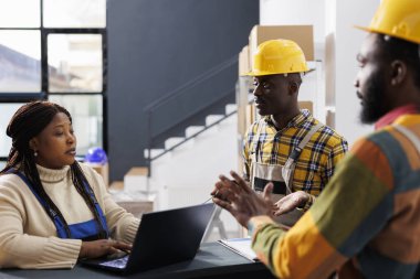 Perakende mağazası çalışanları danışmadaki müşteri siparişleri yönetimini açıklıyor. Tüm siyah depo operatörleri kask takıp depoda depolanan malları tartışıyor.