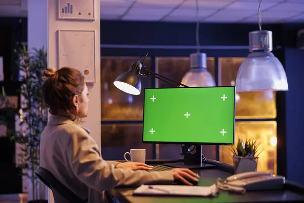 Businesswoman looking at green screen chroma key mock up computer with isolated display, working overtime at company strategy in startup office. Executive manager analyzing financial report growth
