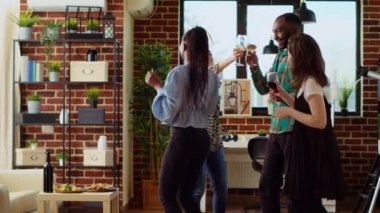 Evde parti veren, oturma odasında dans eden ve elinde şarap kadehleriyle gezen misafirlerin BIPOC karışımı. En iyi arkadaşlar, hafta sonu takılırken, kalçalarını sallarken enerjik ritimlerle dans ederler.