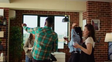 Apartman partisindeki misafirlerin çok kültürlü bir karışımı kahkaha ve dans hareketlerini paylaşıyor, oturma odasında canlı bir atmosfer yaratıyor. Mutlu arkadaşlar hafta sonları elektronik müzik eşliğinde dans ediyorlar.