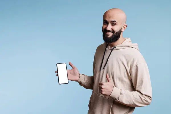 スマートフォンのタッチスクリーン上のスマートフォンのスマートフォンのスマートフォンの笑顔のアラブ人の広告アプリ 空白のモックアップを表示します 空白の画面で携帯電話を表示し 親指のジェスチャーでカメラを見ている陽気な人 — ストック写真