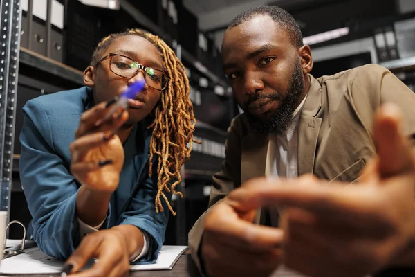 African american man and woman detectives brainstorming and looking at camera. Police investigators partners searching insight for solving crime together in office at night time
