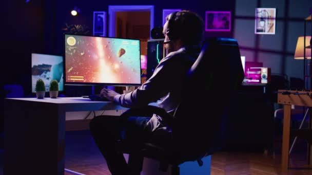 小惑星でレーザーストリームを撮影する宇宙船でシングルプレイヤーのビデオゲームをプレイする暗く照らされたアパートの男 クロスチェアオーバーレイを使用してサイエンスフィクションアーケードゲームのターゲットをヒット — ストック動画