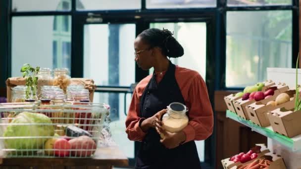 当地超市的非洲裔美国妇女在货架上装上新鲜收获的农产品 邻近的小企业主 店主在可重复使用的容器中摆放食品 — 图库视频影像
