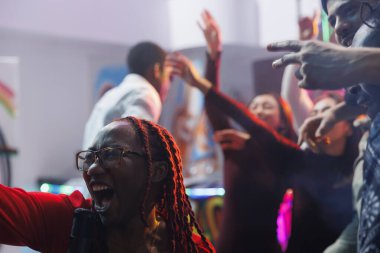 Gece kulübünde arkadaşlarıyla parti yaparken yüksek sesle şarkı söyleyen ve çığlık atan bir kadın. Kaygısız Afro-Amerikan kulüpçüsü kulüpte eğlenirken bağırıyor ve karaokenin tadını çıkarıyor.