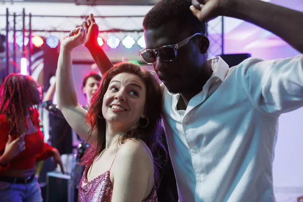 Romantic couple dancing together while relaxing at nightclub party event. Young african american boyfriend and caucasian girlfriend moving on dancefloor, enjoying nightlife
