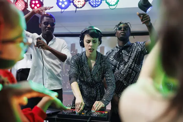 Dj and singers band energetic performance on stage at nightclub disco party. Energetic african american men musicians and caucasian frontwoman playing electronic music live at discotheque