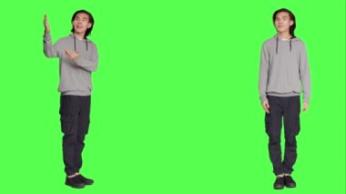 Asyalı kişi yeni reklam kampanyası için sağ ya da sol taraflara işaret ederek stüdyoda pazarlama reklamı üzerinde çalışıyor. Genç erkek model gülümsüyor ve reklamlarda çalışıyor, yeşil ekranın başında duruyor..