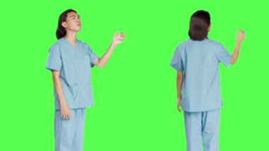 Asyalı tıp asistanı stüdyoda hologramı yeşil ekran düzeni ile görüyor, holografik görüntü ve yapay zeka üzerinde çalışıyor. Sağlık uzmanlığı olan üniformalı bir erkek hemşire..