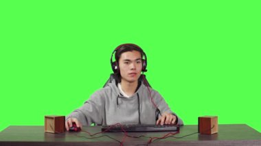 PC masaüstünde oynayan Asyalı adamın POV 'u, tüm yeşil ekran arka planına karşı oturuyor. Genç oyuncu oyun yarışmasında oyuncularla eğleniyor, iş yerinde kulaklık takıyor..