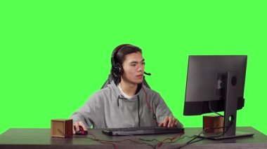 Genç oyuncu bilgisayar masasında oturuyor ve insanlarla web tabanlı video oyunları oynuyor, modern aletleri kullanarak iyi vakit geçiriyor. Asyalı kişi yeşil ekran için RPG yarışmasında yarışıyor.
