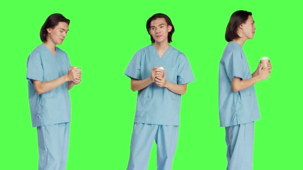 アジアの専門家は グリーンスクリーンの背景にコーヒーカップを楽しんでいます スタジオでホットカフェインリフレッシュメントを飲むヘルスケアの専門知識を持つ男性看護師 制服付き医療アシスタント — ストック動画