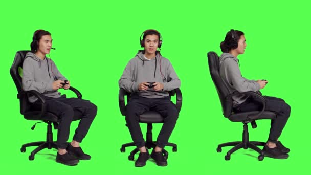 亚洲男子使用控制器竞争 坐在椅子上与全身上下的绿色屏幕在工作室 与他人一起玩网络游戏的年轻人 玩网络游戏的人 — 图库视频影像