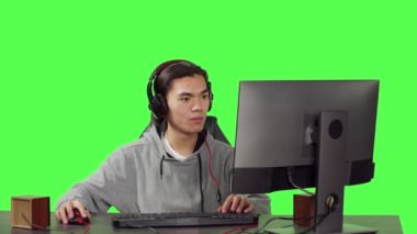 Asyalı bir insan masa başında arkadaşlarıyla online RPG oyunu oynuyor. Genç adam yeni web yarışmasında eğleniyor, yeşil ekran arka planında kulaklık takmış insanlarla konuşuyor..