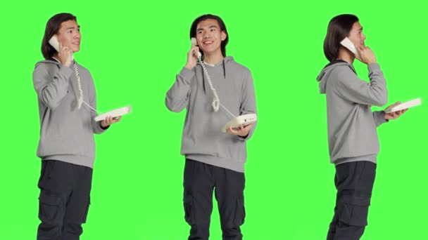 亚洲人通过固定电话交谈 一边站在绿屏背景下一边用绳索接听电话 使用复古电话进行远程通信的年轻人 — 图库视频影像