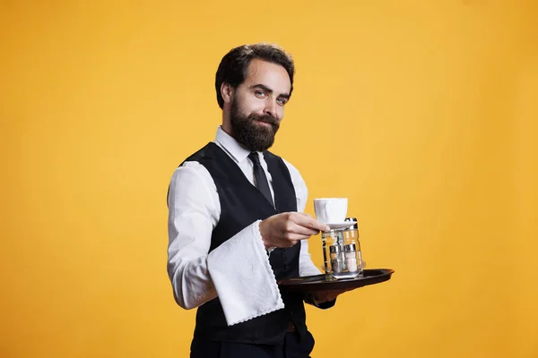 Experienced waiter serving coffee at table, pretending to hand out cup of refreshment for customers. Young adult butler working at luxury restaurant, carrying food tray for catering.