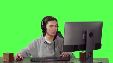 Masa başında oynayan erkek oyuncu, rakipleriyle oynanan RPG video oyunları için online çoklu oyuncu turnuvasıyla eğleniyor. Yalıtılmış yeşil ekran arkaplanı üzerinden Asyalı adam oyunu.