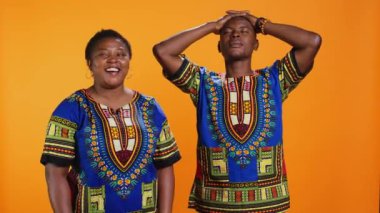 Neşeli karı koca kamerada birlikte gülüyorlar, turuncu arka planda aptalca şakalar yapıyorlar. Afro-Amerikan çifti eğlenceli anlar yaşıyor, kaygısız insanlar gülüyor..