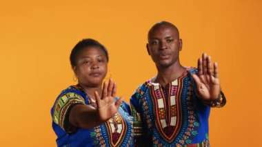 Afrika kökenli Amerikalı çift avuç içi ile dur işareti yapıyor, olumsuzluklarını dile getiriyorlar ve turuncu arka planda reddedildiklerini belirtiyorlar. Etnik evliler bir şeyden memnun değil, uyarı işareti..