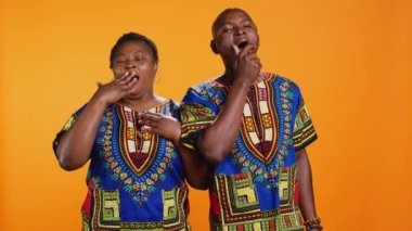 Bitkin düşmüş karı koca kamera karşısında esniyorlar, tükenmişlikle uğraşıyorlar ve son derece yorgun hissediyorlar. Afro-Amerikalı çift turuncu arka planda uyuyakalıyor, uykulu insanlar..