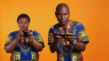 Etnik çift telefondaki mobil video oyunlarıyla eğleniyor, kameradaki online oyun turnuvasına katılıyorlar. Afrika kökenli Amerikalı erkek ve kadın akıllı telefondan oyun yarışmasında oynuyorlar..