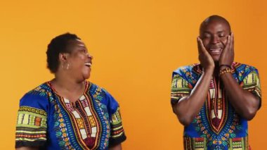 Mutlu Afro-Amerikan halkı stüdyoda bir şeye gülüyor, şakalarla eğleniyor ve turuncu arka planda eğleniyor. Evli çift kameraya gülüyor, aptal ortaklar..