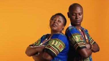 Kaygısız, rahat, kamera önünde poz veren, sırt sırta verip geleneksel renkli kıyafetler giyen etnik bir çift. Afro-Amerikalı insanlar turuncu arka planda kendilerini güvende ve neşeli hissediyorlar..